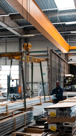 Warehouse employee operating crane to lift stack of aluminium profiles.